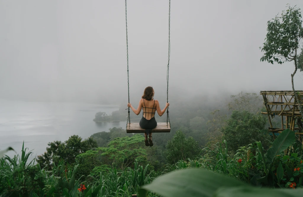 Woman sitting on a swing overlooking a foggy, lush jungle landscape in Bali, capturing a serene and adventurous moment